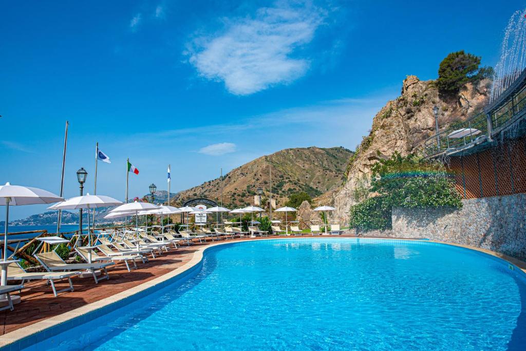 une piscine avec chaises et parasols dans un complexe hôtelier dans l'établissement Baia Taormina - CDSHotels, à Forza dʼAgro