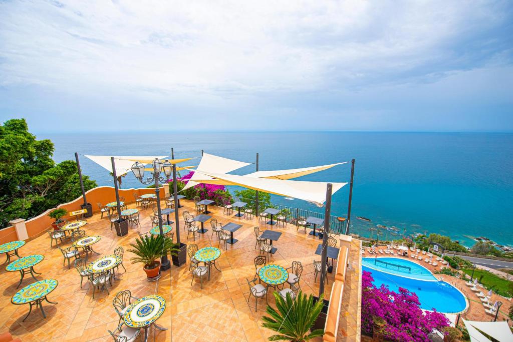 un patio extérieur avec tables et chaises et une piscine dans l'établissement Baia Taormina - CDSHotels, à Forza dʼAgro 105 autres photos
