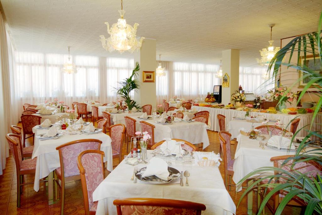 un restaurant avec des tables et des chaises blanches et un lustre dans l'établissement Hotel Victoria, à Bibione