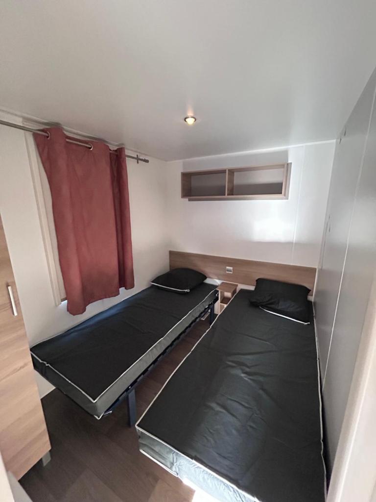 Cette petite chambre comprend 2 lits et un rideau rouge. dans l'établissement Mobil Home 2 chambres, 4 à 6 personnes, Vias Plage, Camping La Carabasse - 4 étoiles, à Vias