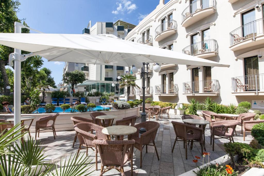 d'une terrasse avec des tables et des chaises sous un parasol blanc. dans l'établissement Hotel Ambassador, à Rimini