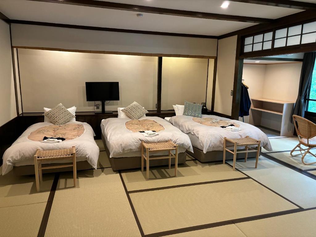 Cette chambre comprend 2 lits, des chaises et une télévision. dans l'établissement Kusatsu Onsen Kusatsu Hotel1913, à Kusatsu