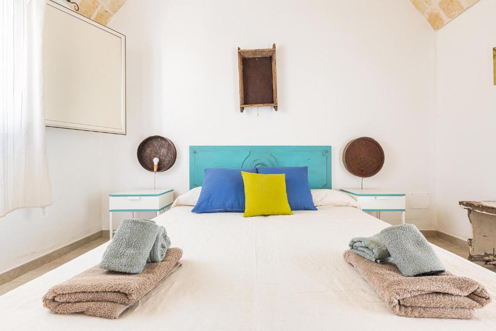 - une chambre dotée d'un grand lit blanc avec des oreillers bleus et jaunes dans l'établissement Trullo Fico by Perle di Puglia, à San Michele Salentino
