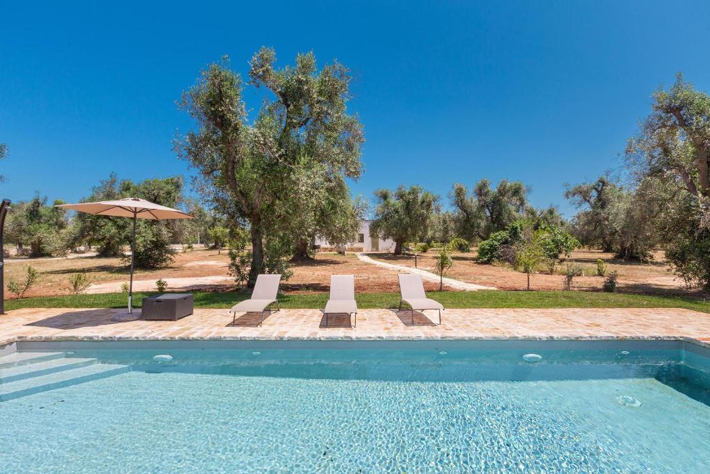 une piscine avec deux chaises et un parasol dans l'établissement Trullo Fico by Perle di Puglia, à San Michele Salentino
