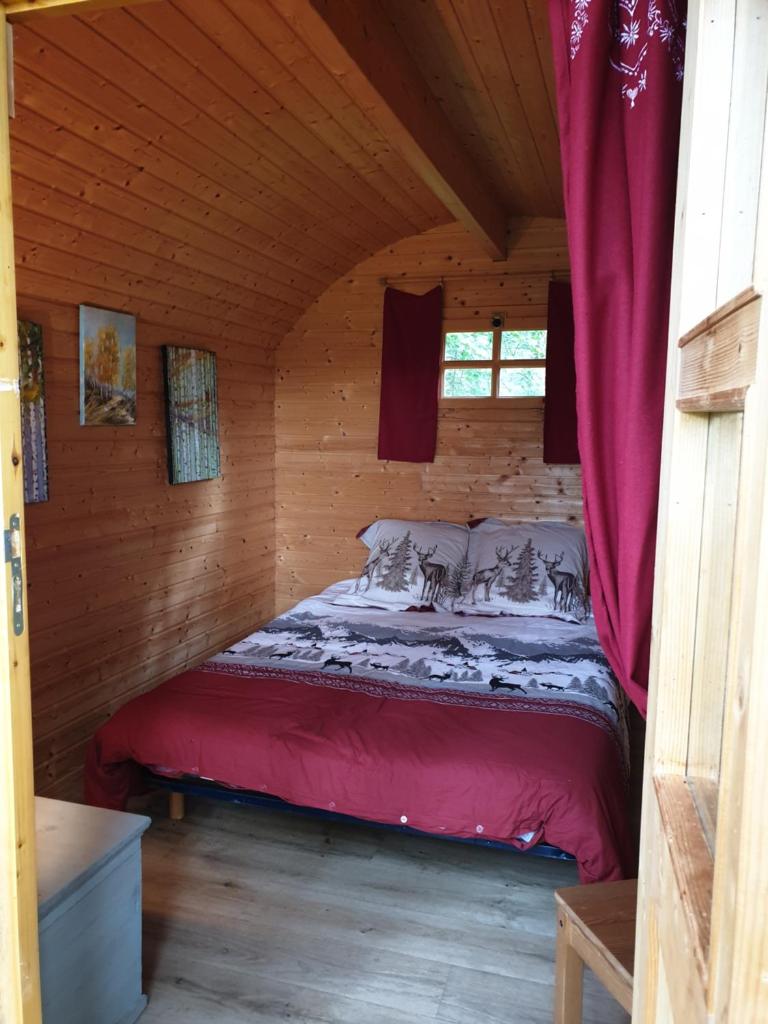 Ce lit se trouve dans une cabane en rondins dotée de rideaux rouges. dans l'établissement White wood lodge, à Nonville