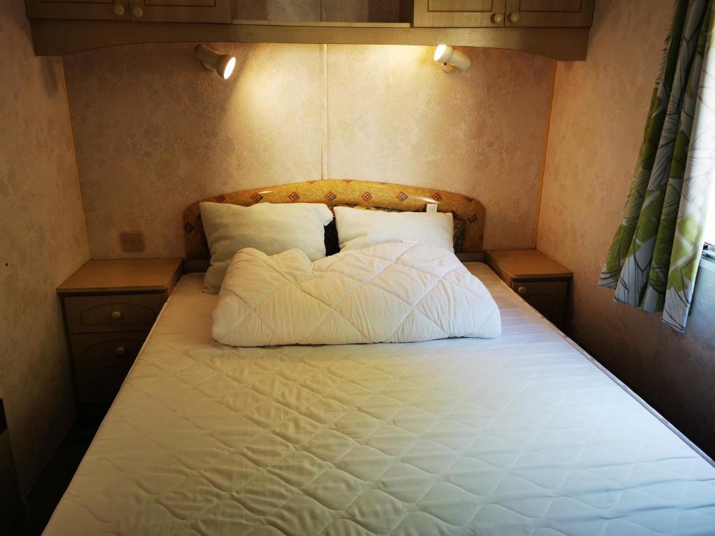 un lit avec des draps blancs et des oreillers dans une chambre dans l'établissement Bungalow camping 3 étoiles, à Chazelles-sur-Lyon
