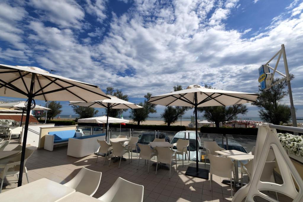 une terrasse avec des tables blanches, des chaises et des parasols dans l'établissement Hotel Ancore, à Senigallia