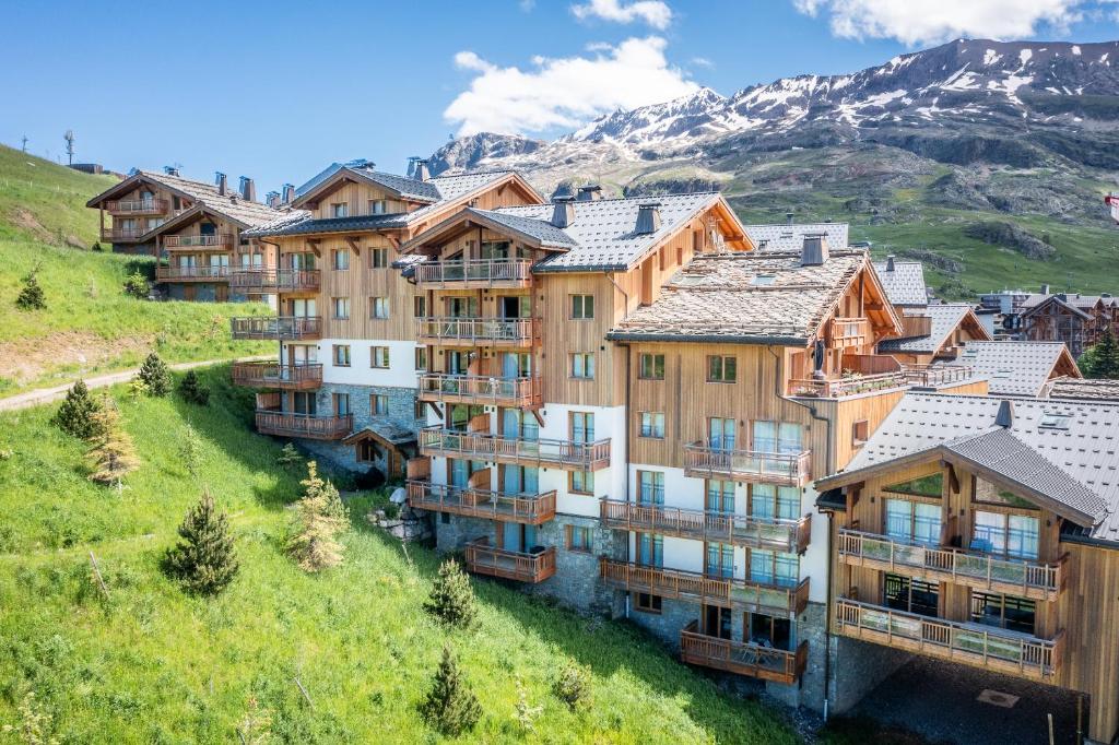 un immeuble situé sur une colline avec des montagnes en arrière-plan dans l'établissement Residence Hameau de Clotaire Alpe d'Huez - by EMERALD STAY, à L'Alpe-d'Huez