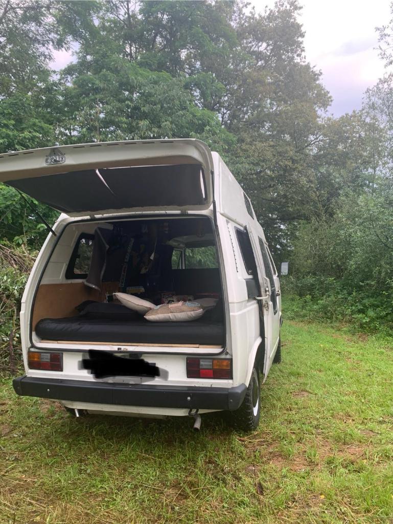 une camionnette blanche garée dans l'herbe avec sa porte ouverte dans l'établissement Nuit en van au bord étang privé, à Saint-Sauveur