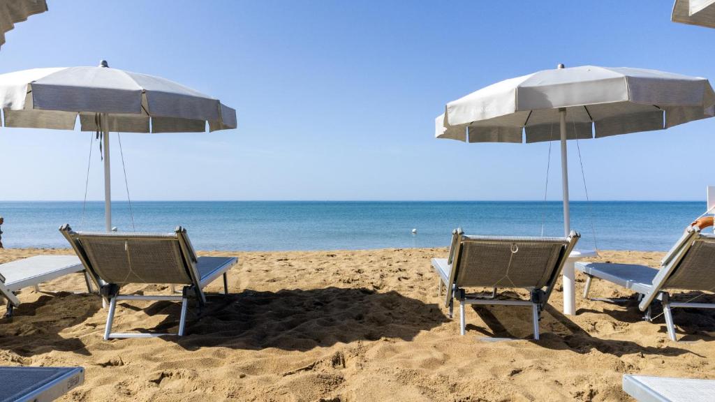 deux chaises et parasols sur une plage avec l'océan dans l'établissement Mangia's Selinunte Resort, à Marinella di Selinunte