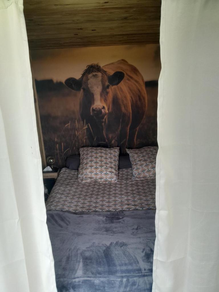 une chambre avec un lit orné d'une peinture de vache dans l'établissement cabane amazonia, à Litteau