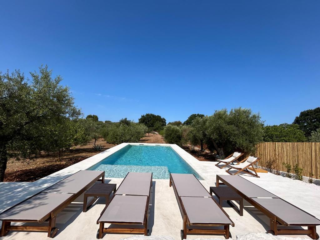 une piscine avec des bancs et une personne assise sur une chaise dans l'établissement Trulli Biancopumo - private pool, à Monopoli