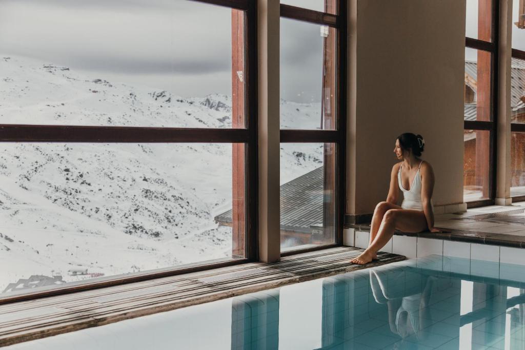 une femme assise sur un rebord de fenêtre à côté d'une piscine dans l'établissement Résidence Les Balcons de Val Chavière, à Val Thorens