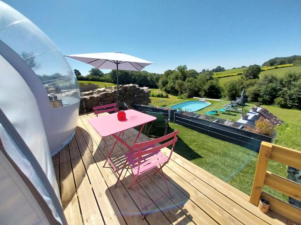 une terrasse avec une table et des chaises roses ainsi qu'un parasol dans l'établissement La Bubble, à La Salvetat-Peyralès