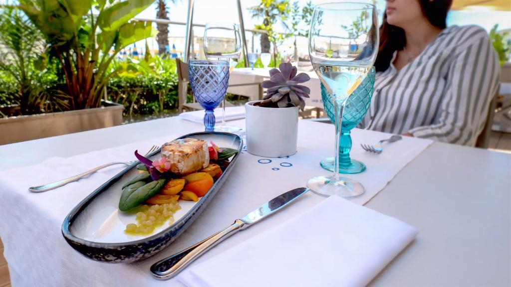 une table avec une assiette de nourriture et un verre de vin dans l'établissement Hotels Vidi Miramare & Delfino, à Lido di Jesolo