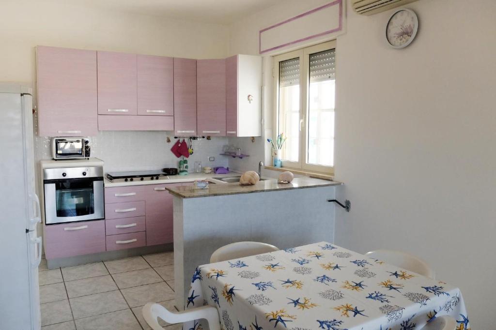 une cuisine avec des placards roses et une table avec des chaises dans l'établissement Villa Il Giardino con Piscina a soli 350 mt dalla Spiaggia di Punta Prosciutto, à Punta Prosciutto