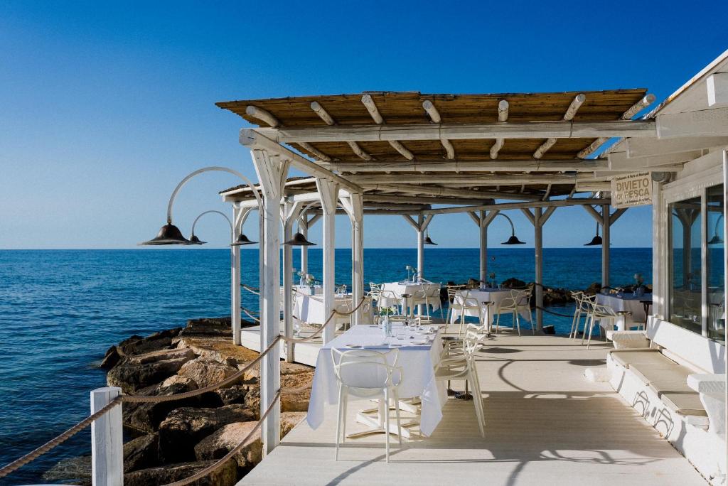 un restaurant avec des tables et des chaises blanches sur l'eau dans l'établissement La Peschiera, à Monopoli