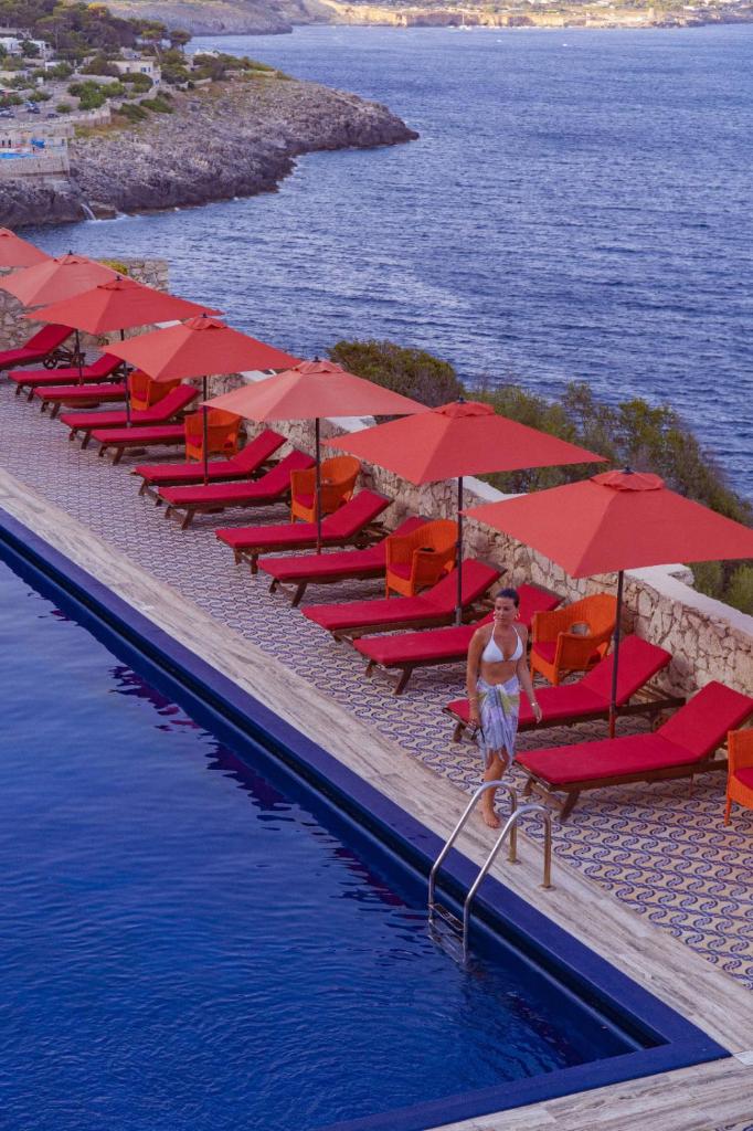 une femme debout à côté d'une piscine avec parasols rouges dans l'établissement Hotel Piccolo Mondo, à Castro di Lecce