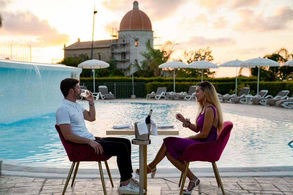 deux personnes assises sur des chaises au bord d'une piscine en train de boire du vin dans l'établissement Sentido Michelizia Tropea Resort, à Tropea