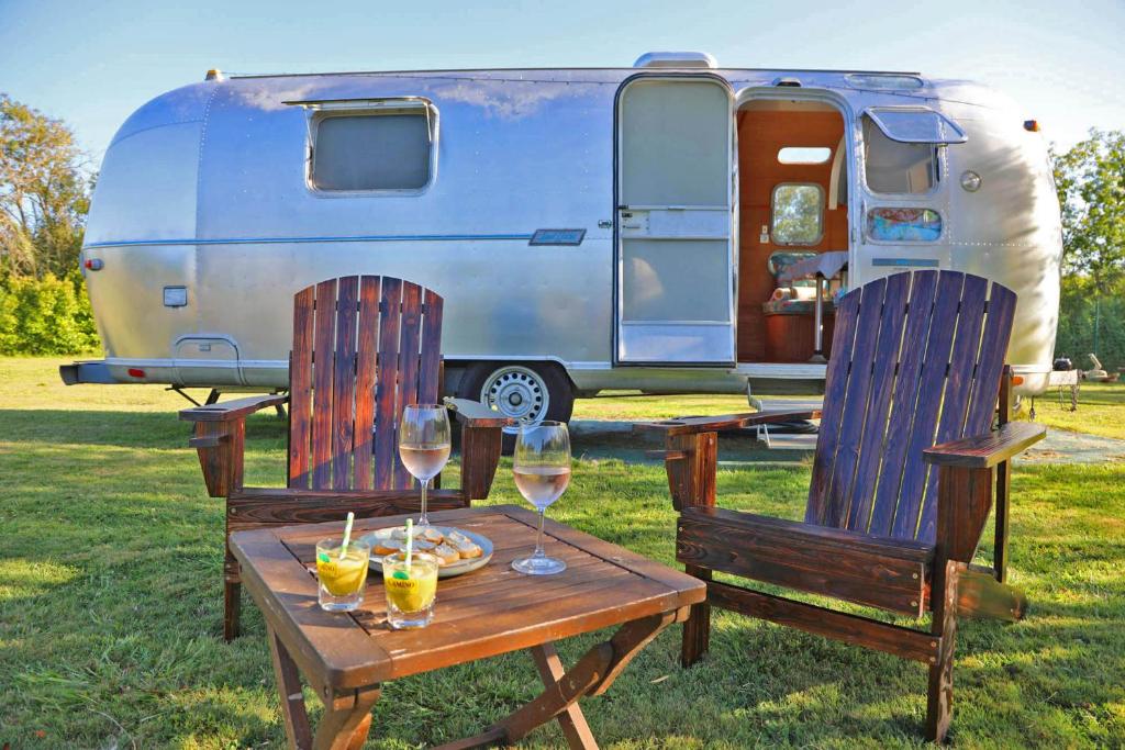 une table et deux chaises avec des verres à vin et une remorque dans l'établissement Caravane Airstream bord de lac, à Saint-Loubès