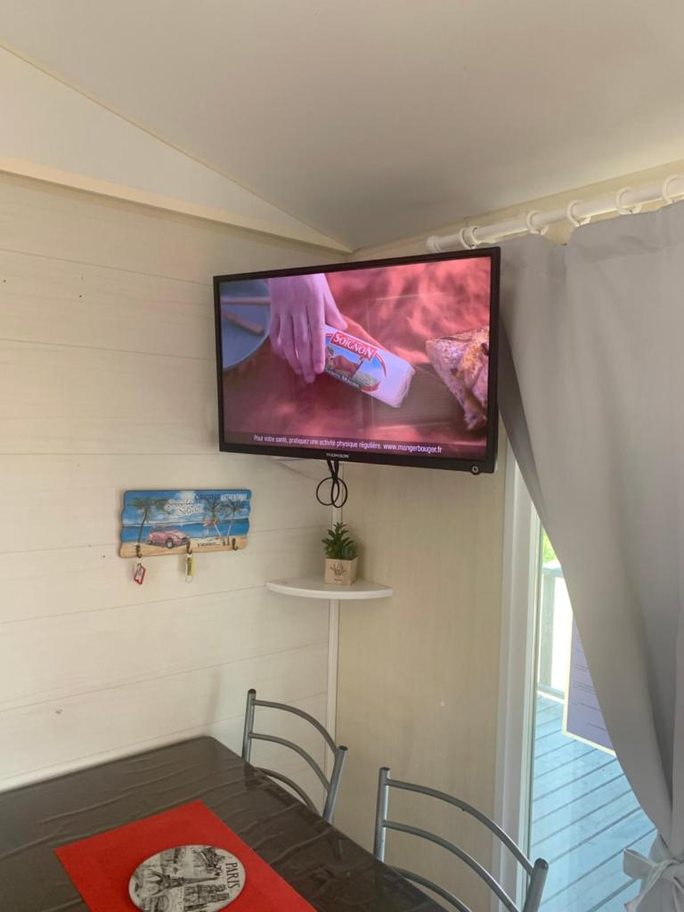 une télévision suspendue sur un mur avec une table et des chaises dans l'établissement Flo mobil home camping Poney trois étoiles route de Moustiers Ste Croix, à Sainte-Croix-de-Verdon