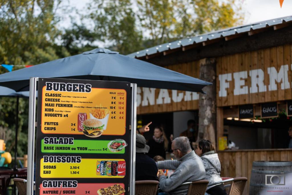 un panneau de menu devant un restaurant avec des personnes assises dans l'établissement Cabane trappeur 4pers à la ferme aventure du perthus, à Le Perthus