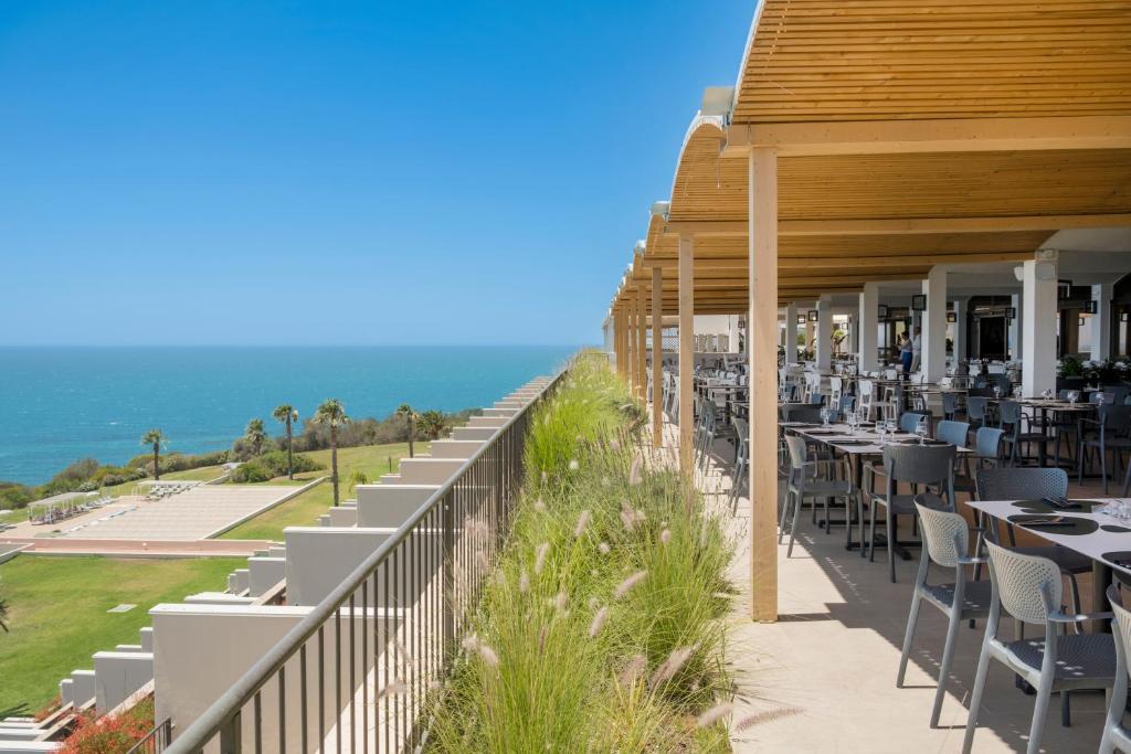 un restaurant avec des tables et des chaises et l'océan dans l'établissement Mangia's Torre Del Barone Resort & SPA, à Sciacca