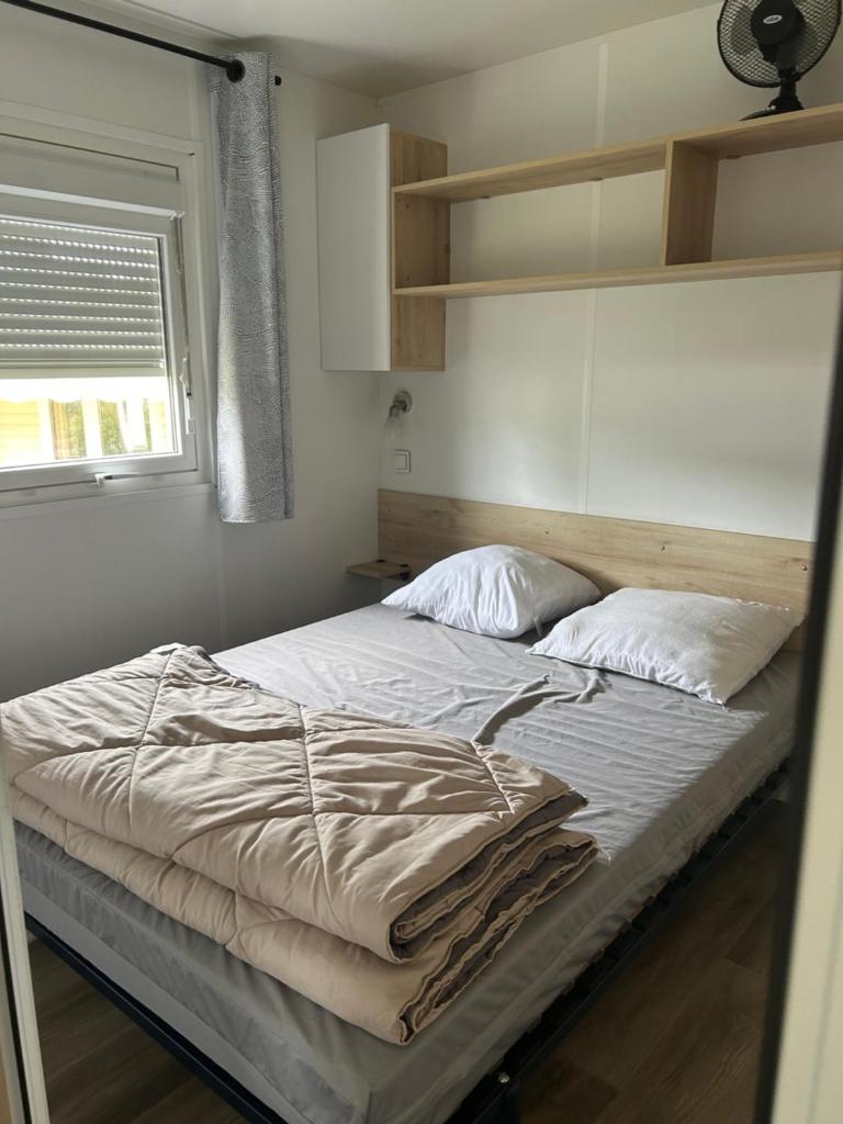 - une chambre dotée d'un grand lit avec des draps blancs et une fenêtre dans l'établissement Camping Les Viviers chez So Claouey, à Lège-Cap-Ferret