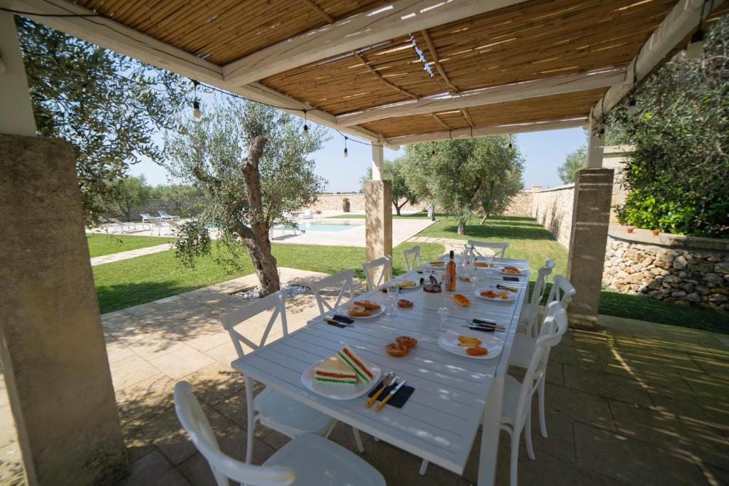 une grande table blanche avec des chaises blanches sous un toit en bois dans l'établissement Lisària Villa Delle Meraviglie With Pool, à Castrignano deʼ Greci