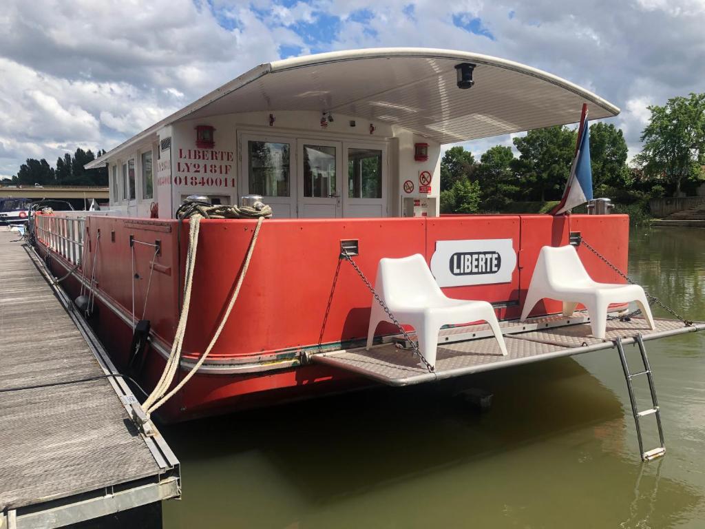 un bateau avec deux chaises assises sur le quai dans l'établissement Péniche Design 115m2 Port Privé Vue Seine à 15min de Paris, à Asnières-sur-Seine