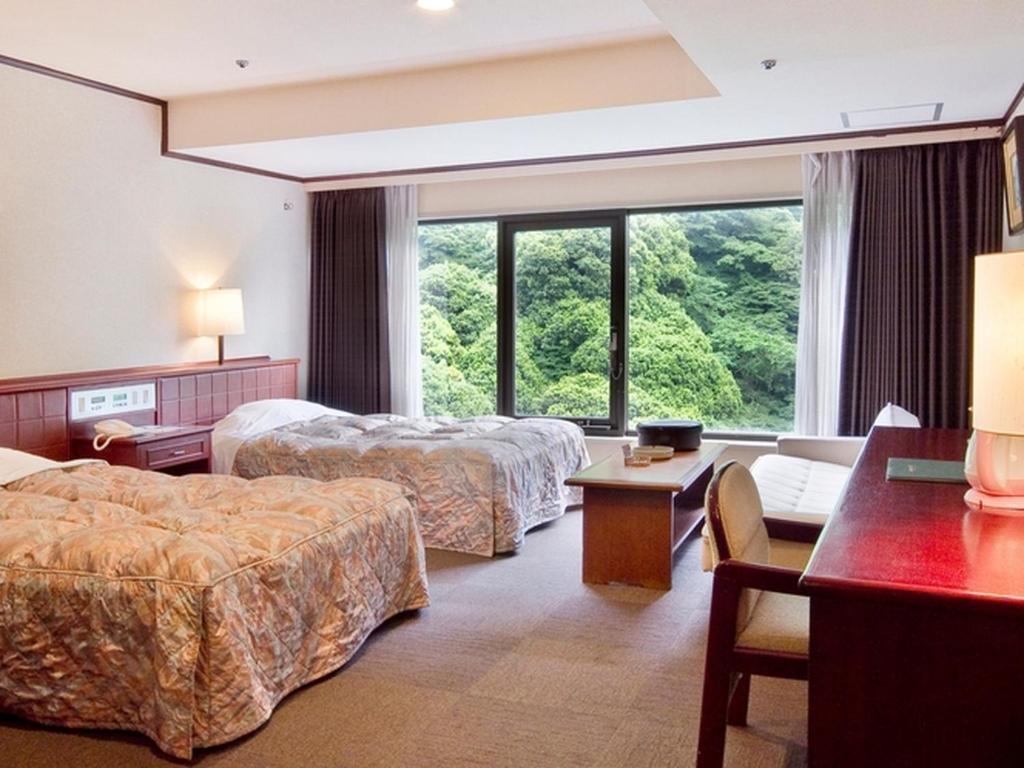 une chambre d'hôtel avec deux lits et une fenêtre dans l'établissement Okudogo Ichiyunomori, à Matsuyama