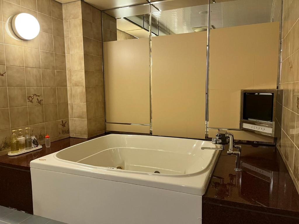 une grande baignoire blanche dans une salle de bain avec une télévision dans l'établissement オーラリゾート四條畷, à Shijonawate