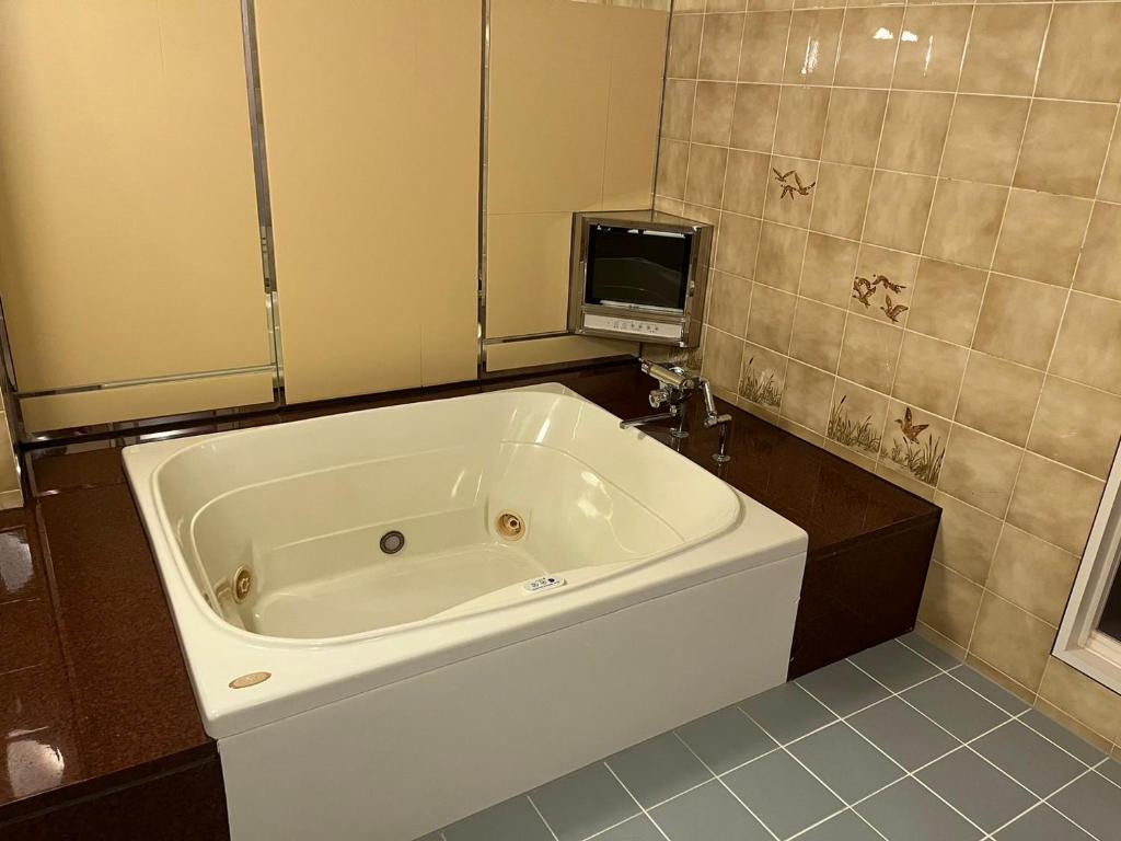 une grande baignoire blanche dans une salle de bain avec une télévision dans l'établissement オーラリゾート四條畷, à Shijonawate