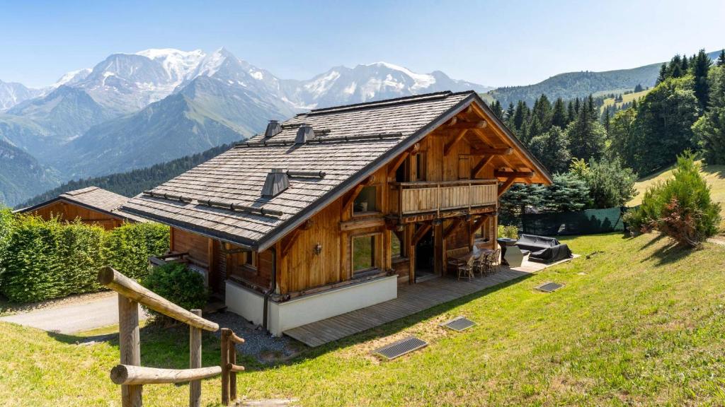 une maison sur une colline avec des montagnes en arrière-plan dans l'établissement Chalet Vallée de Chamonix Randonnées, Rafting et Spa, à Saint-Gervais-les-Bains