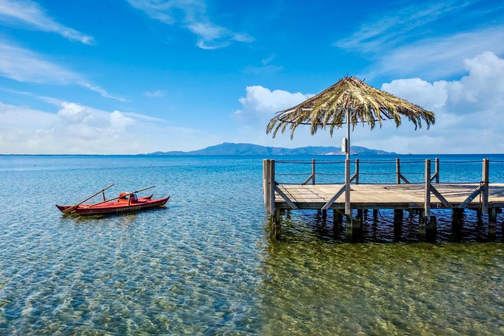 un bateau à côté d'un quai avec un parasol en paille dans l'établissement Residence with pool and private beach in Talamone just 500 mt from the sea, à Talamone 21 autres photos