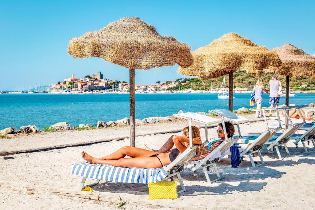 - deux femmes sur des chaises longues sur une plage avec parasols dans l'établissement ISA - Residence with pool and private beach in Talamone just 500 mt from the beach, à Talamone