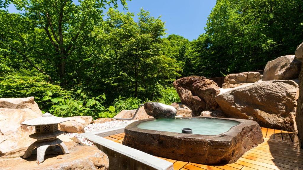 une fontaine en pierre sur une terrasse en bois avec des rochers dans l'établissement Mogamitakayu Zenshichinoyu Ohira, à Zao Onsen
