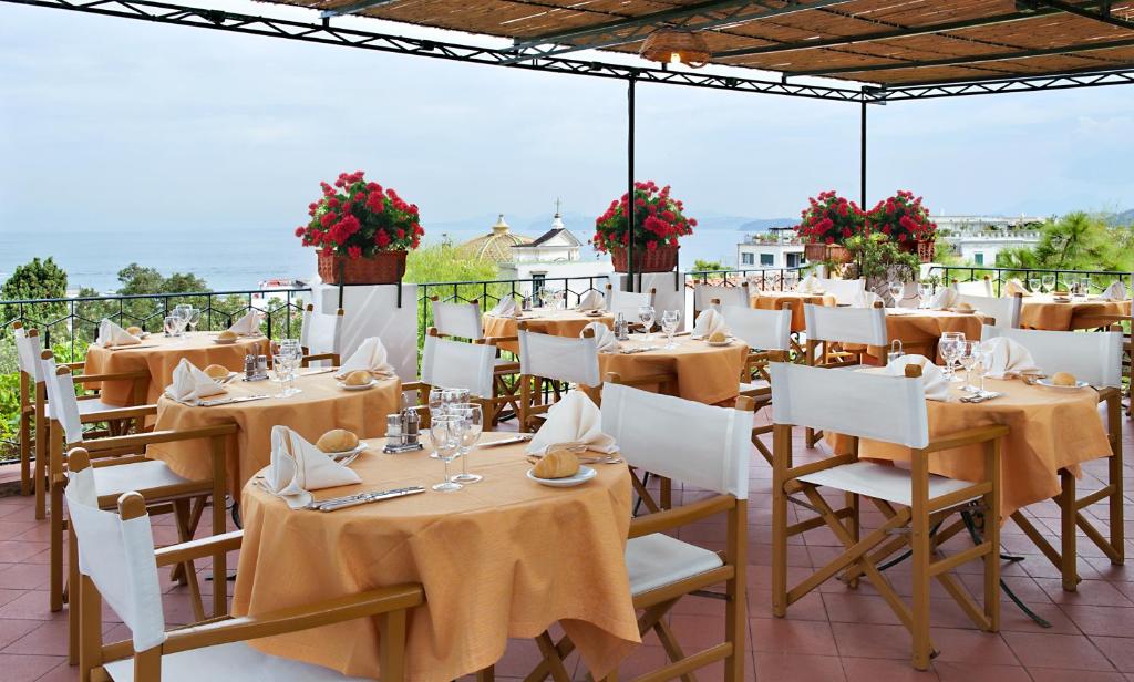 un restaurant avec des tables, des chaises blanches et des fleurs dans l'établissement Hotel La Villarosa Terme, à Ischia