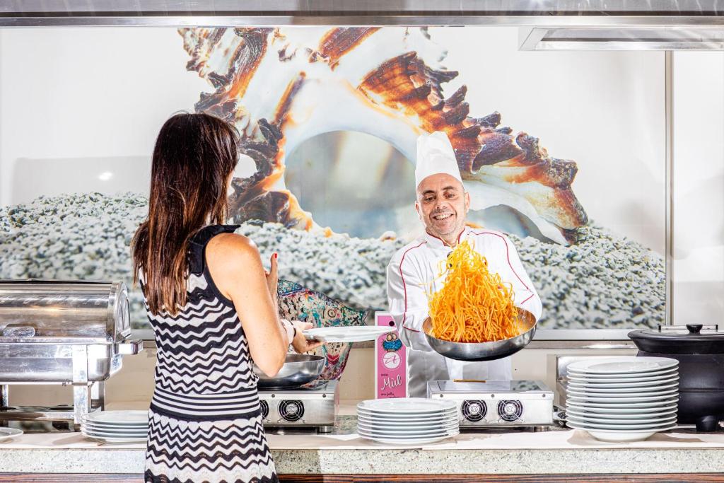 une femme debout dans une cuisine avec un chef préparant la nourriture dans l'établissement Hotel Eden, à Bibione