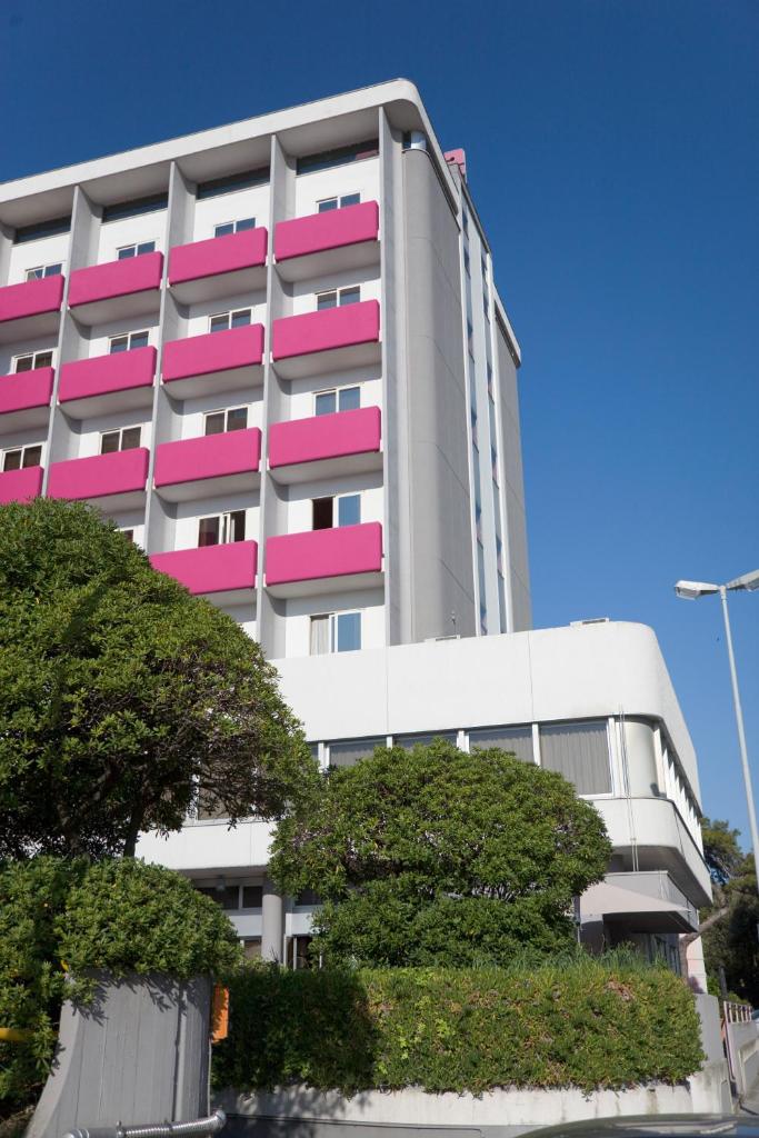 un bâtiment blanc et rose avec des arbres devant lui dans l'établissement SenB Hotel, à Senigallia