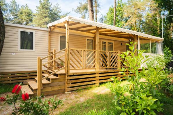 une cabane en bois avec une terrasse couverte et une maison dans l'établissement Camping Officiel Siblu Bois de Bayadène, à Piriac-sur-Mer