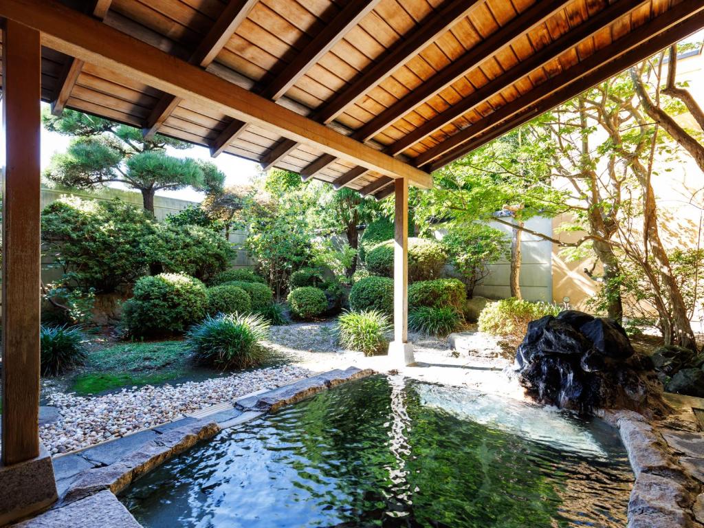 un jardin avec un étang sous une pergola en bois dans l'établissement Tabist Chikuba Shinyotei Hakodate Yunokawaonsen, à Hakodate