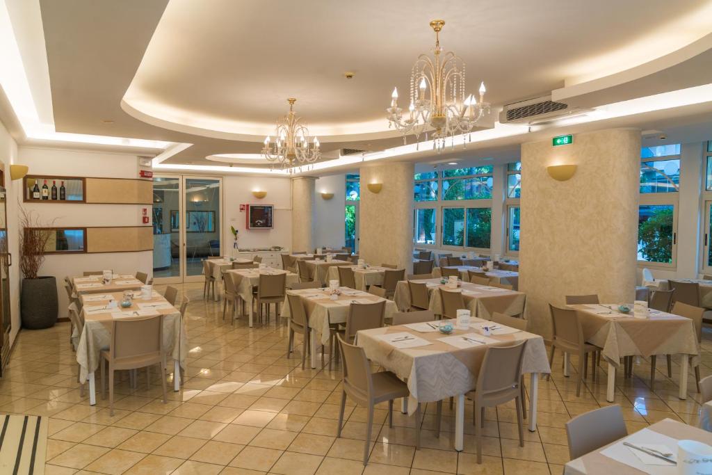 un restaurant avec des tables et des chaises blanches et des lustres dans l'établissement Hotel Europa Milano Marittima, à Milano Marittima