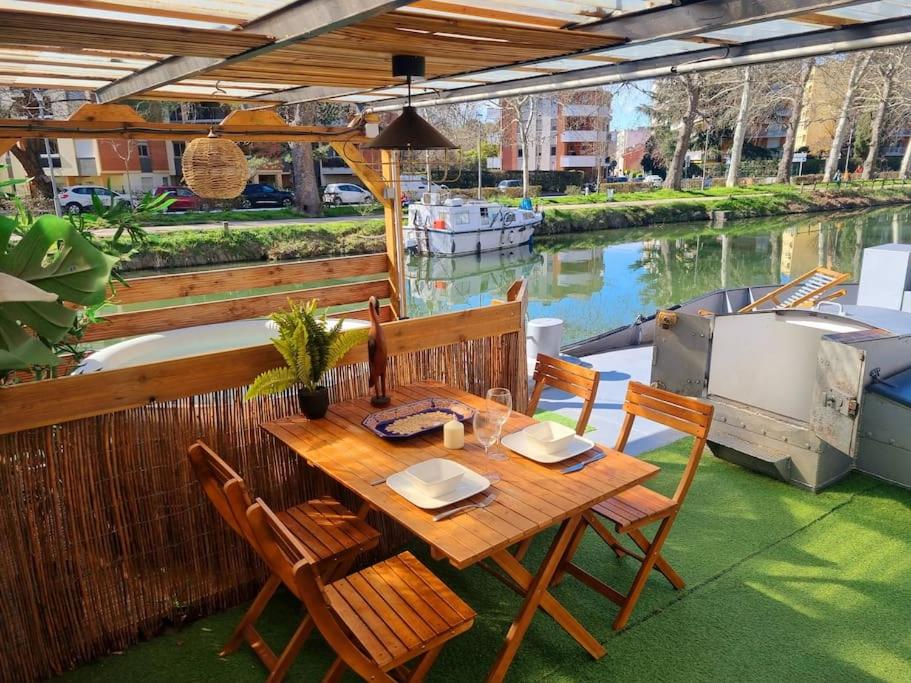 - une table et des chaises en bois sur une terrasse avec un bateau dans l'établissement Péniche Chaleureuse avec jacuzzi Toulouse centre, à Toulouse