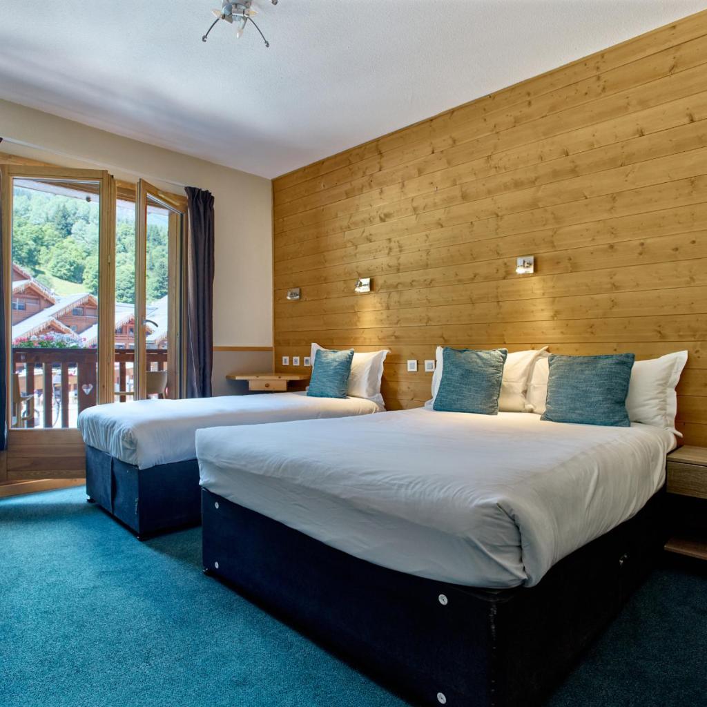 deux lits dans une chambre d'hôtel avec une fenêtre dans l'établissement Hôtel Les Grangettes, à Méribel