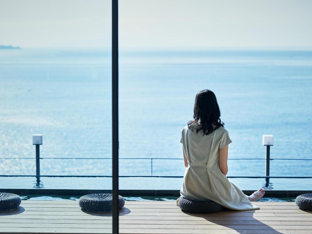 une femme assise sur un quai qui regarde l'eau dans l'établissement Atami Izusan Karaku, à Atami