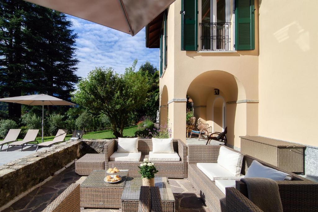 une terrasse avec des canapés, des chaises et un parasol dans l'établissement Villa Riva - by MyHomeInComo, à Lenno
