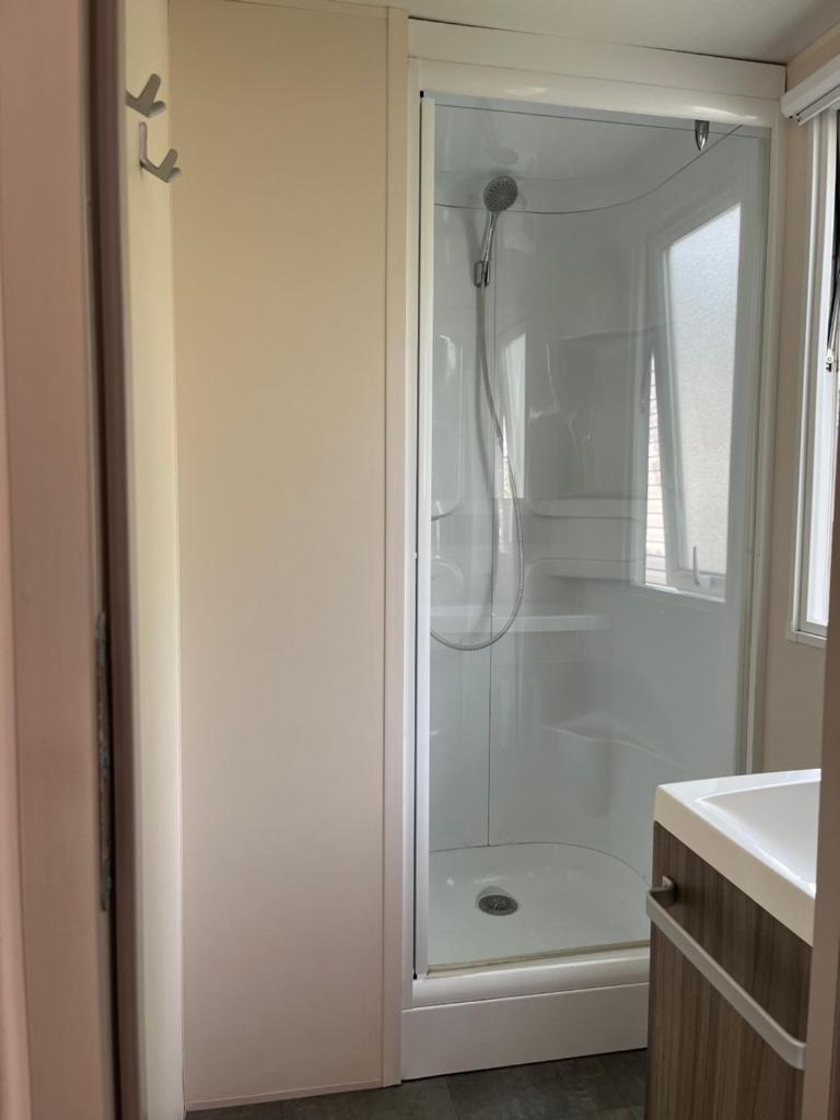 La salle de bains est pourvue d'une douche et d'un lavabo blanc. dans l'établissement Mobil home en Vendée, à Angles