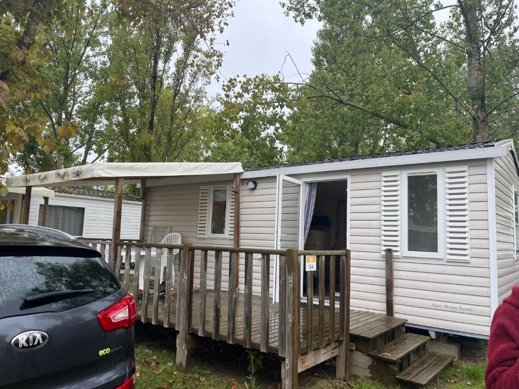 Une petite maison blanche avec une véranda et une voiture dans l'établissement Mobil home en Vendée, à Angles
