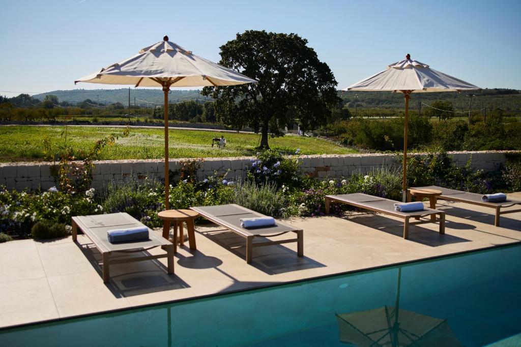 une piscine avec deux tables et deux parasols dans l'établissement Tenuta Giotta, à Castellana Grotte